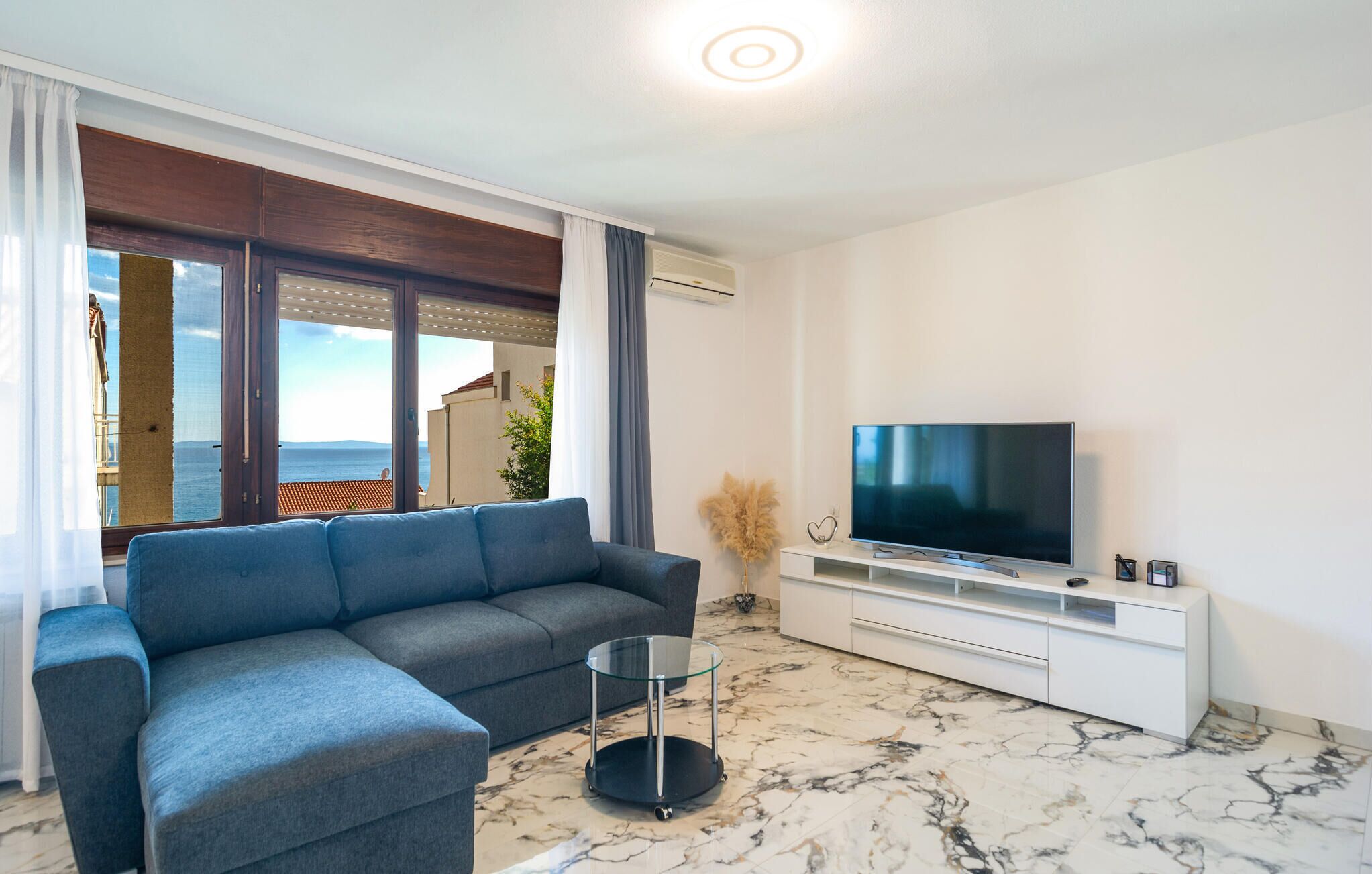 A modern living room with a sofa, TV, and a view of the sea.