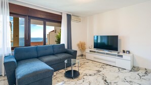 En moderne stue med sofa, fjernsyn og havudsigt.