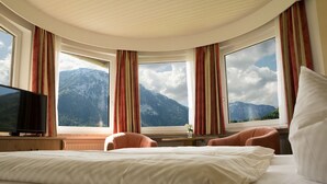 A hotel room with a large bed, two armchairs, a TV, and a view of mountains through large windows. - Apartment 4, 44sqm, 2 balconies, 1 bedroom, living room, kitchen, WLAN, TV (Ruhpolding)