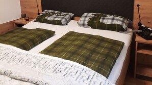 En snyggt bäddad säng med grönt och vitt rutigt sänglinne, en vit, fluffig pläd och en sänggavel i trä.