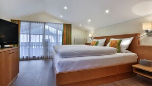 A hotel room with a large bed, a television, a bedside table, and a lamp.