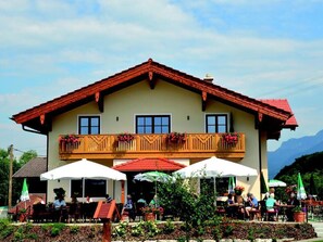 A two-story building with a balcony, outdoor seating, and a mountain backdrop.