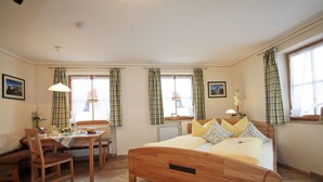 Un dormitorio con una cama de madera, una mesa de comedor con sillas y una ventana con cortinas escocesas.