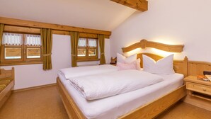 A bedroom with a wooden bed, two windows with curtains, a nightstand, and a wooden ceiling beam. - (07) Zwei-Raum-Ferienwohnung (Reit im Winkl)