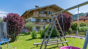 A wooden chalet with a balcony, surrounded by a well-maintained garden and a swing set. - (07) Zwei-Raum-Ferienwohnung (Reit im Winkl)