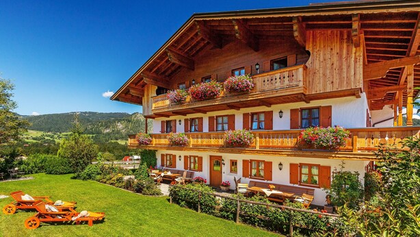 A traditional wooden building with multiple balconies, outdoor seating, and a well-maintained garden. - (07) Zwei-Raum-Ferienwohnung (Reit im Winkl)