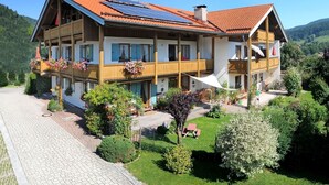 A two-story chalet with a red-tiled roof, balconies with flower boxes, and a paved driveway.