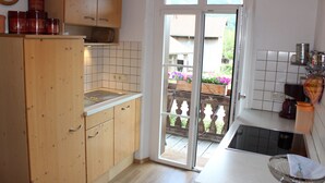 Una cocina con armarios de madera, un lavamanos y una ventana que da a un balcón lleno de flores.