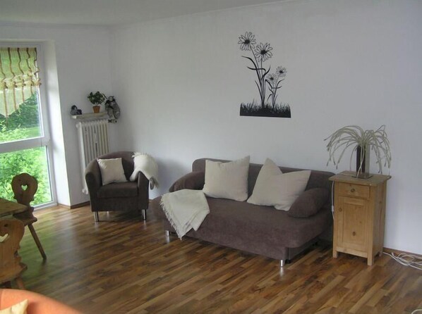 Relax in this inviting living room with a sofa, cabinet, and wall art, set against a large window and wooden floor.