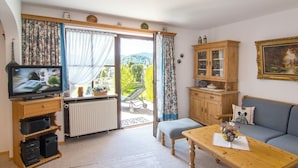 Una sala de estar acogedora con televisor, armarios de madera, un sofá y vistas al exterior.