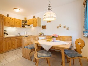 A kitchen with wooden cabinets, a dining table with blue cushioned chairs, and a hanging light fixture.
