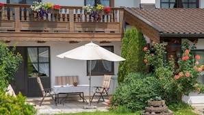 Un patio con una mesa y sillas, un paraguas blanco y un jardín con flores y arbustos.