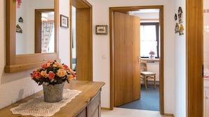 Un pasillo con un aparador de madera, un espejo y un jarrón de flores. Hay dos puertas que dan a otras habitaciones.