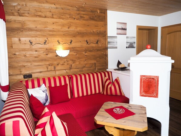 Um quarto aconchegante com parede de madeira, sofá listrado de vermelho, pequena mesa de madeira e porta branca.