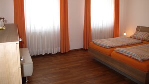 Hotellihuone, jossa on kaksi sänkyä, puulattia ja oranssit verhot.