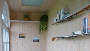 A cozy room with a blue sofa, wooden shelves with books, a small plant, and a picture on the wall. - Ferienwohnung 65 qm, für 2-4 Personen, 2 getrennte Schlafzimmer, Balkon u. Nichtraucher (Schönau am Königssee)