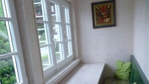 A room with a bench against the wall, a small table, and a window with a view of greenery outside. - Ferienwohnung 65 qm, für 2-4 Personen, 2 getrennte Schlafzimmer, Balkon u. Nichtraucher (Schönau am Königssee)