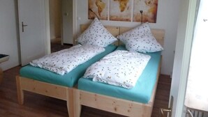 A double bed with a wooden frame and teal bedding, two pillows with a floral pattern, and a world map artwork above the bed. - Ferienwohnung 65 qm, für 2-4 Personen, 2 getrennte Schlafzimmer, Balkon u. Nichtraucher (Schönau am Königssee)