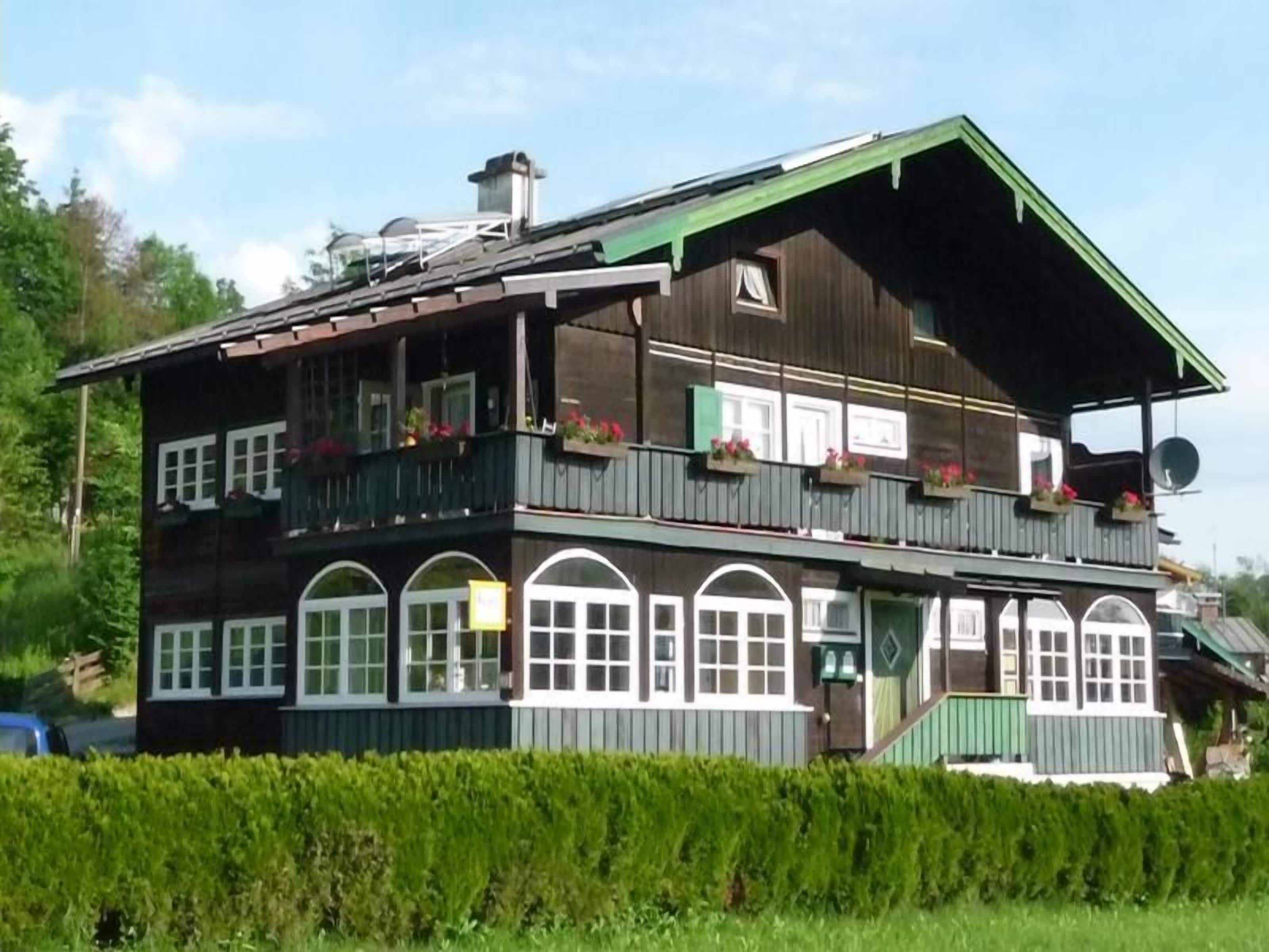 A two-story wooden building with balconies, large windows, and a green roof.