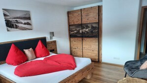 A bed with a wooden frame, red pillows, and a white bedspread. - Three-room vacation apartment 52sqm time-out, 2 extra bedrooms, kitchen, balcony (Reit im Winkl)