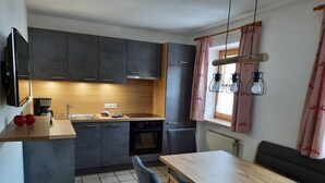 A compact kitchen with dark cabinets, a wooden countertop, a built-in oven, and a dining area with a table and chairs. - Three-room vacation apartment 52sqm time-out, 2 extra bedrooms, kitchen, balcony (Reit im Winkl)