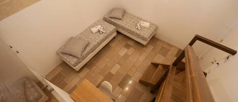 A small, compact room with two single beds, a wooden table, and a chair.