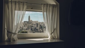 Una ventana con cortinas blancas, con vista a un casco antiguo y una torre destacada.