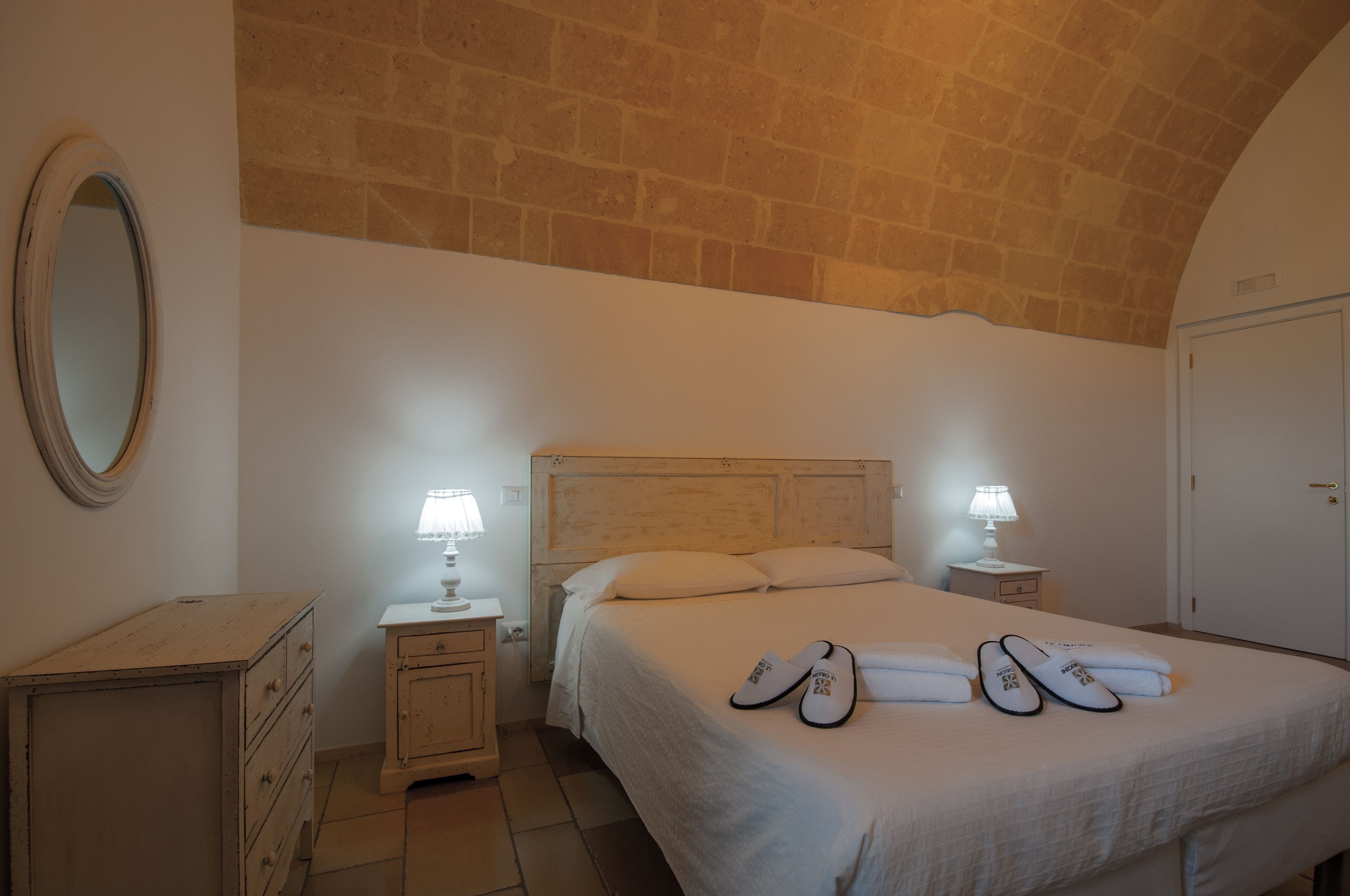 A bedroom with a bed, two bedside tables, a dresser, a mirror, and a wardrobe.