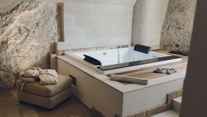 Un baño moderno con una bañera grande, un banco y una pared de piedra.
