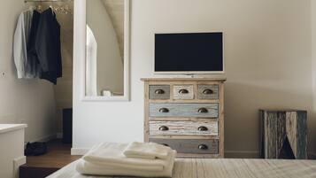 Une chambre à coucher avec un lit, une commode à tiroirs, un téléviseur posé sur le dessus et un miroir accroché au mur.