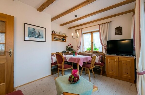 A cozy dining area with wooden beams, a TV, and a table set with chairs.