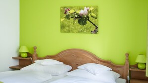 Un lit double avec du linge de lit blanc, une tête de lit en bois et deux tables de chevet avec des lampes vertes.