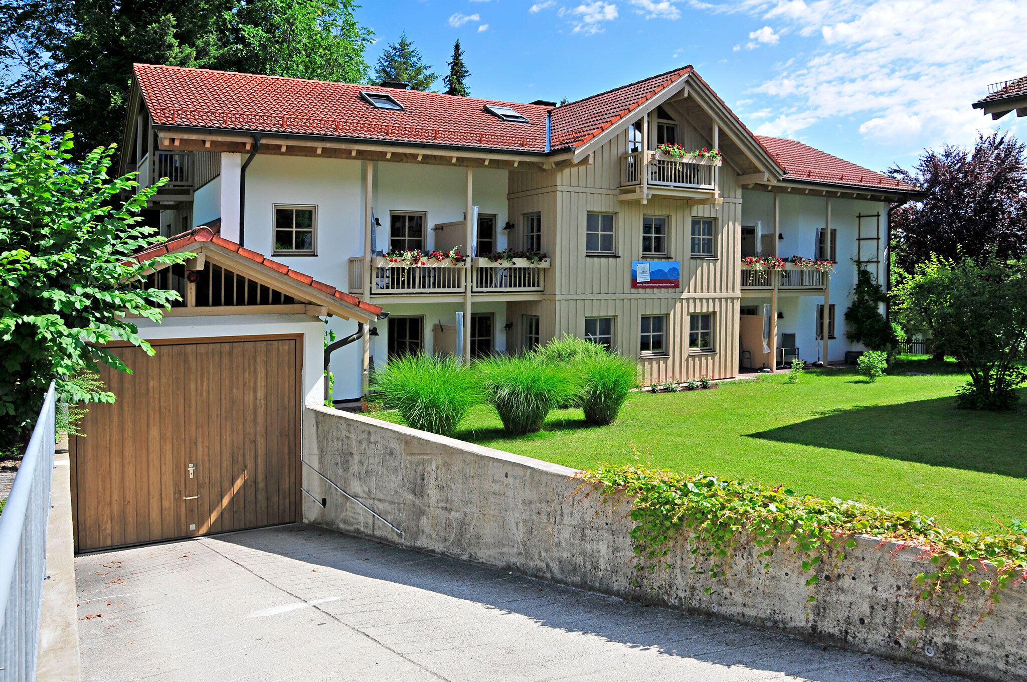 A multi-story building with a red-tiled roof, balconies with flower boxes, and a well-maintained lawn.