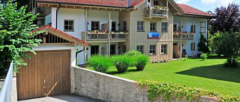 A multi-story building with a red-tiled roof, balconies with flower boxes, and a well-maintained lawn.