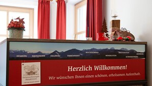 Un comptoir d’accueil avec une pancarte de bienvenue, une photo encadrée d’un village de montagne et une composition décorative comprenant un verre, une pomme de pin et des ornements.
