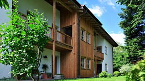 Un bâtiment en bois à deux étages, doté de balcons, d’une cour verdoyante et entouré d’arbres.