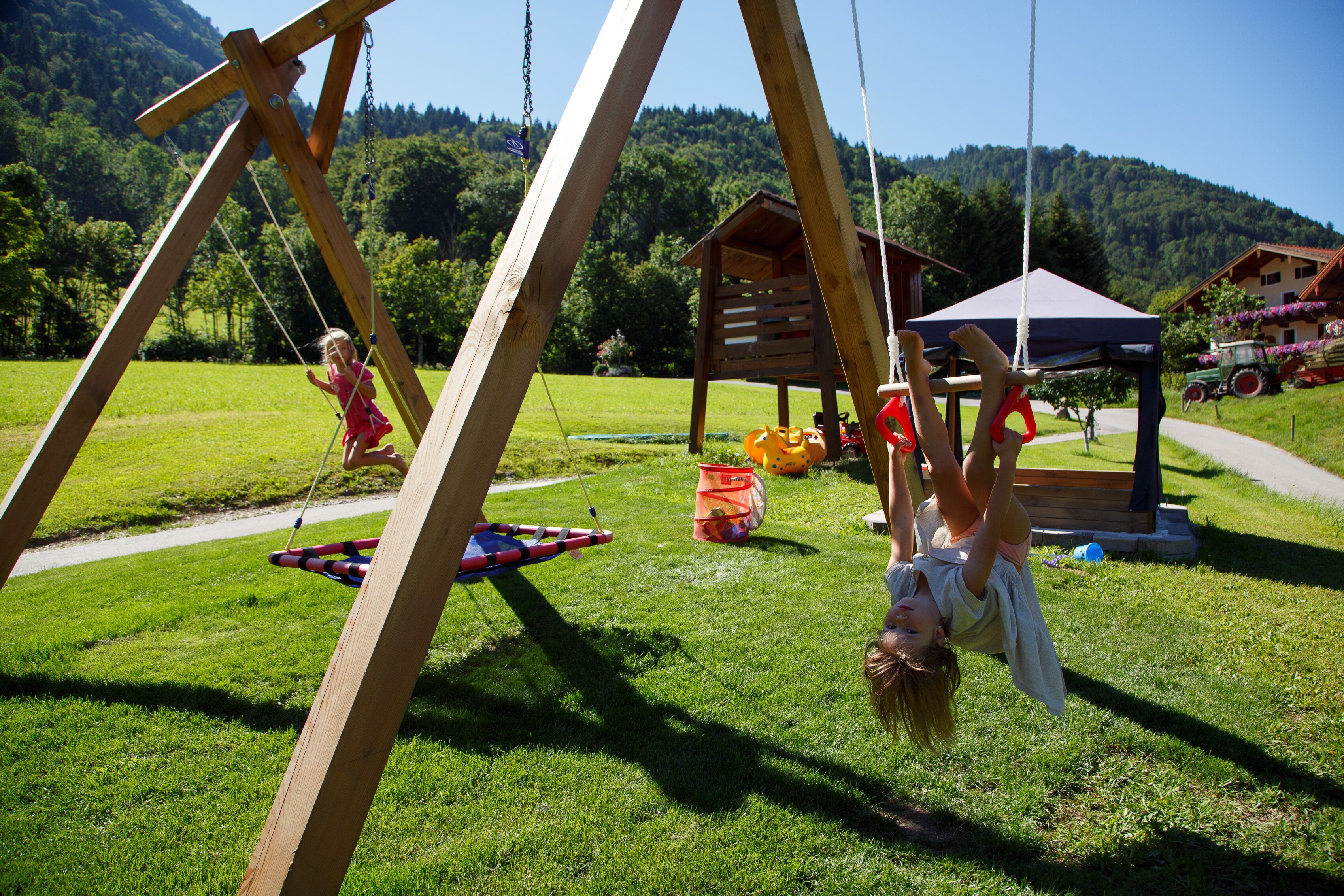A wooden swing set in a grassy area with a wooden structure in the background.