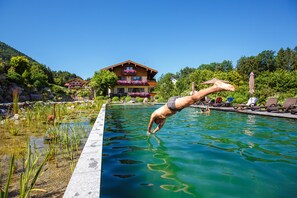 A swimming pool with a person diving into it, surrounded by lounge chairs and a building with balconies. - 9. vacation apartment Berganemone, 89sqm, balcony, kitchen, 2 bedrooms, 1 living room (Ruhpolding)