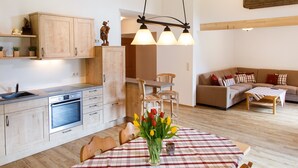 A modern kitchen with wooden cabinets, a built-in oven, and a dining area with a table set for two. - 9. vacation apartment Berganemone, 89sqm, balcony, kitchen, 2 bedrooms, 1 living room (Ruhpolding)