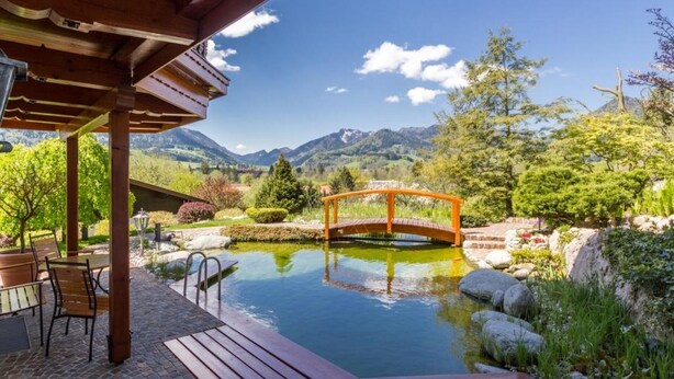Una terraza de madera con piscina, un puente de madera y vistas a la montaña.