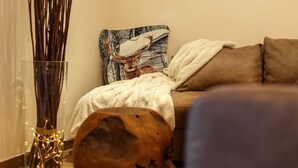 Una sala de estar acogedora con un sofá, un cojín decorativo con un ciervo, un florero de vidrio con ramas y un cuenco de madera.