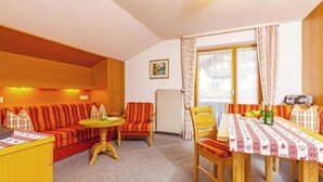Une pièce confortable avec un canapé, une petite table et une table à manger avec des chaises. Il y a une fenêtre avec des rideaux et un radiateur au mur.