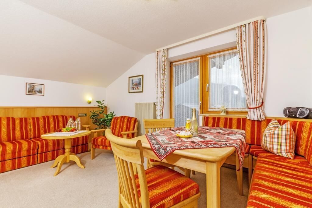 Une pièce chaleureuse avec un canapé en bois, une petite table ronde et une table à manger recouverte d’une nappe rouge.