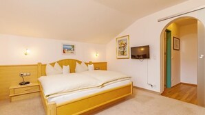 Une chambre à coucher avec un lit en bois, des tables de chevet, une télévision et une porte donnant sur une autre pièce.
