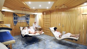 Ein Zimmer mit Holzboden und schrägen Wänden, einem Massagetisch und einer Person, die ein Buch liest.