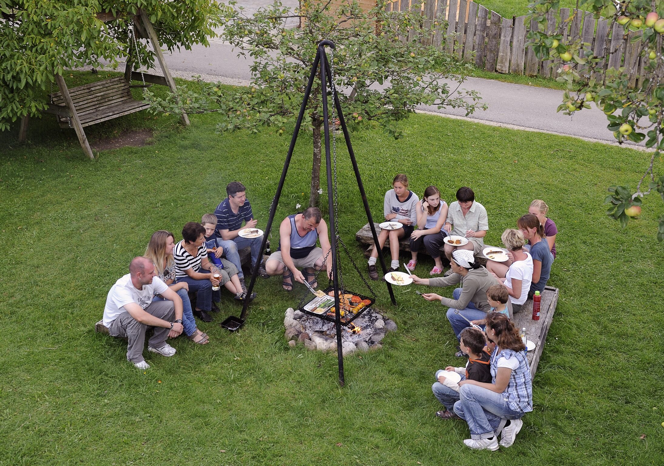 A group of people sitting around a campfire in a grassy outdoor area.