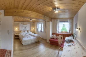 Une pièce chaleureuse avec un plafond en bois, un lit, un canapé rouge, une table avec des livres et une fenêtre avec des rideaux.