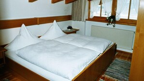 Une chambre à coucher avec un lit en bois, une table de chevet, une fenêtre avec des rideaux et un radiateur.