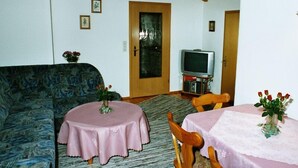 Un salon comprenant un canapé, un téléviseur et deux tables ornées de centres de table floraux.