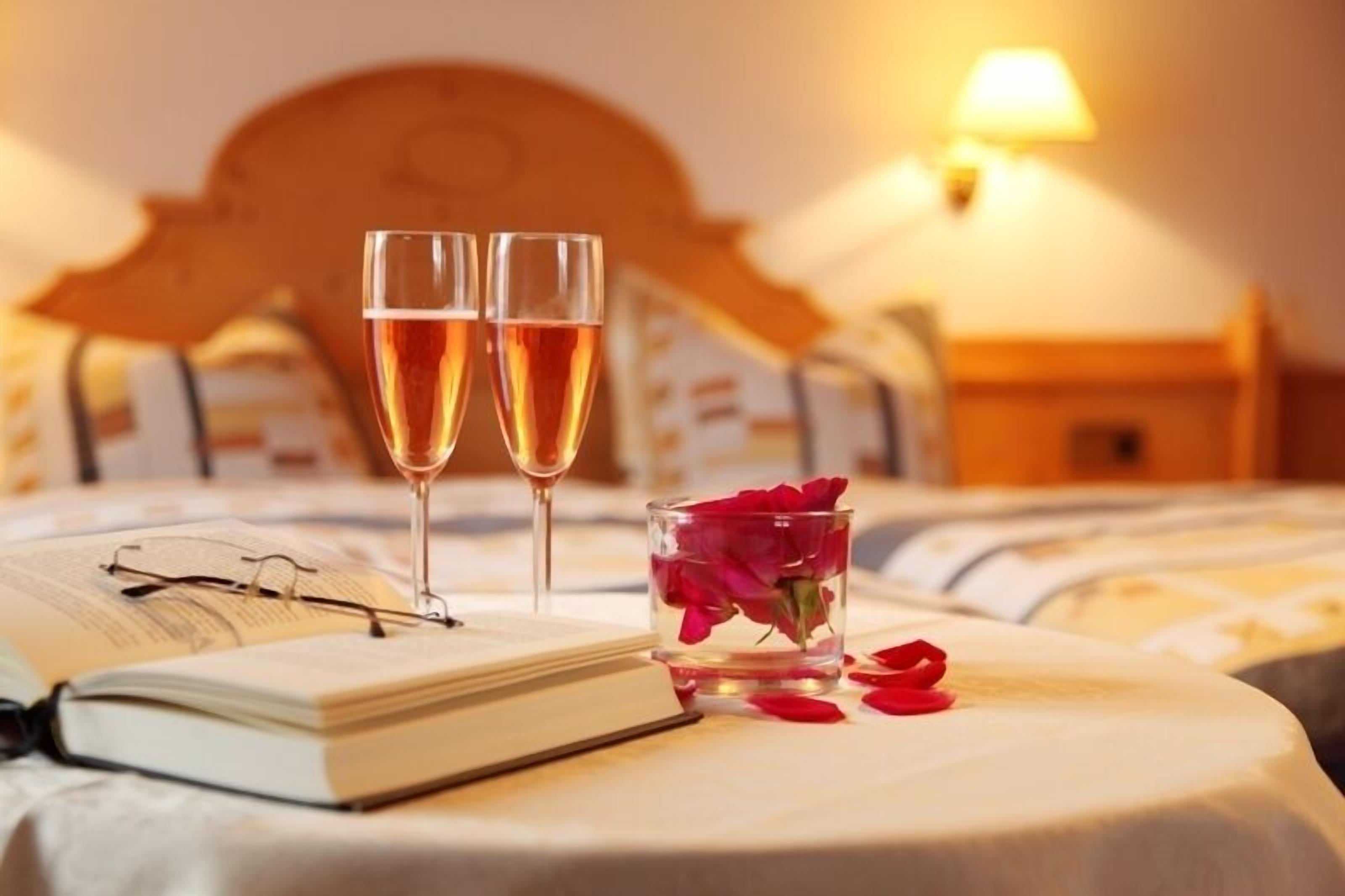 A neatly made bed with a wooden headboard, a bedside table with a lamp, and two glasses of a clear beverage on a bedside table.